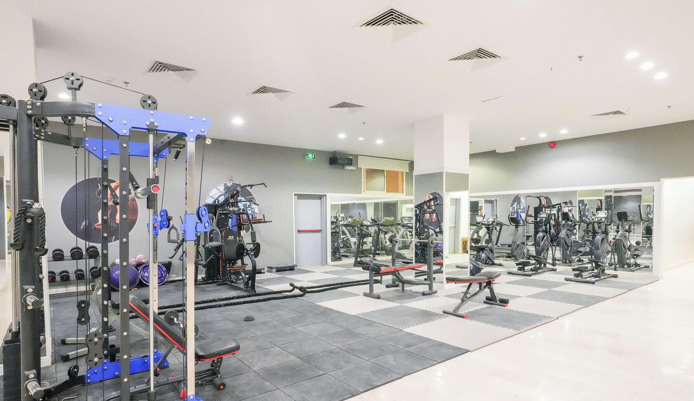Een sportschool met diverse fitnessapparaten, krachttoestellen en een spiegelwand.