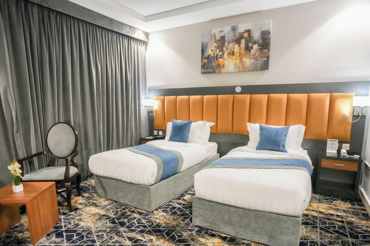Habitación de hotel con dos camas, una silla, una mesita y un cuadro en la pared.