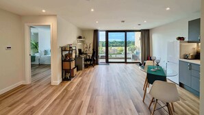 A modern apartment with a spacious living area, a balcony with a city view, and a kitchen with a refrigerator and cabinets. - Charming Flat Near London Attractions (Sheerwater)