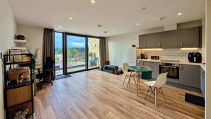 A modern apartment with a spacious living area, a balcony with a view, a kitchen with grey cabinets, and a dining area with a table and chairs. - Charming Flat Near London Attractions (Sheerwater)