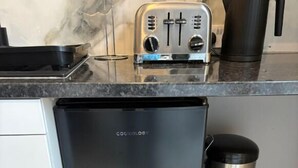 Une cuisine avec un réfrigérateur noir, une machine à café et une poubelle en acier inoxydable.