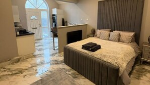 A bedroom with a large bed, a bedside table, a headboard, and a view of the kitchen and living area. - The Norwich Hideaway - Private Hot Tub (Bawburgh)