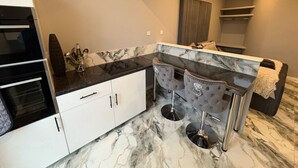 Une cuisine moderne dotée de plans de travail en marbre, de deux tabourets de bar et d’un four encastré.