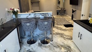A modern kitchen with marble countertops, a central island with bar stools, and a built-in oven. - The Norwich Hideaway - Private Hot Tub (Bawburgh)