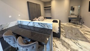 A modern bedroom with a marble vanity, a bed with a fluffy blanket, a grey upholstered chair, and a large mirror above the vanity. - The Norwich Hideaway - Private Hot Tub (Bawburgh)