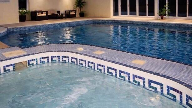 An indoor swimming pool with a tiled edge, wooden beams on the ceiling, and a seating area with chairs and potted plants. - The Norwich Hideaway - Private Hot Tub (Bawburgh)
