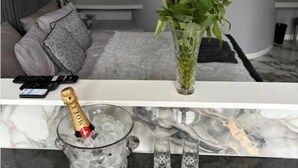 A modern living room with a grey sofa, a glass vase with pink and white flowers, a bottle of champagne, and two glasses on a marble countertop. - The Norwich Hideaway - Private Hot Tub (Bawburgh)