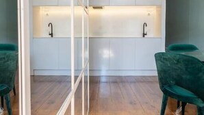 A modern kitchen with white cabinets, a wooden floor, and a green chair. - Clube Charming Apartments - Ribeira (Porto)