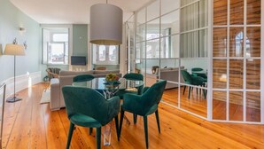 A modern living room with a glass dining table, green chairs, and a large window. - Clube Charming Apartments - Ribeira (Porto)