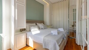 A large bed with white linens, a wooden floor, and a view of a room with a green wall and white curtains. - Clube Charming Apartments - Ribeira (Porto)