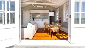 An open-plan living area with a sofa, dining table, and chairs, a kitchen in the background, and a large window. - Clube Charming Apartments - Ribeira (Porto)