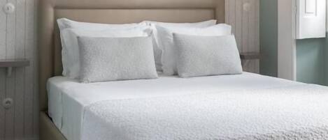 A neatly made bed with white linens and pillows, a wooden headboard, and two wall-mounted light fixtures.