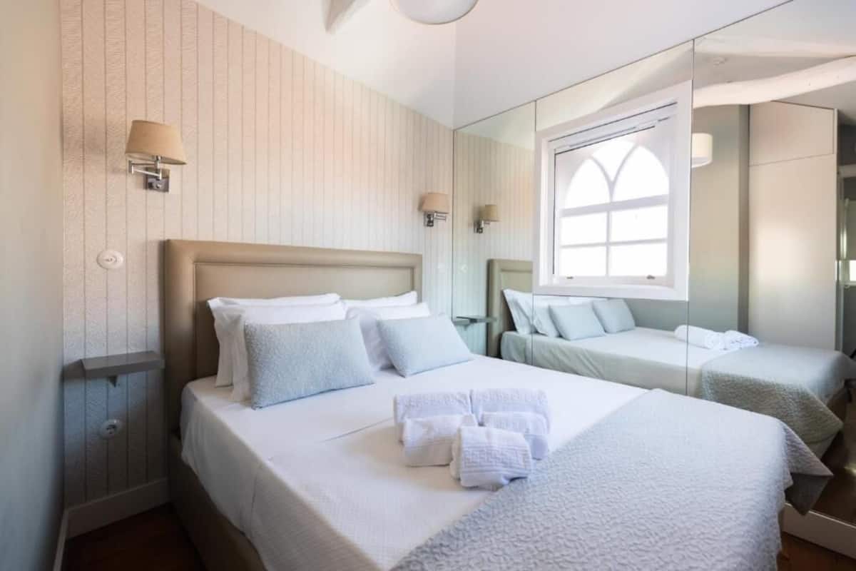 Una habitación de hotel con una cama grande, dos camas más pequeñas, un espejo y una ventana con vistas.