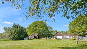 A spacious grassy yard with a large tree, a small wooden shed, and a house with a white facade and dark roof. - Fewhurst Cottage Annex - Billingshurst (Billingshurst, Horsham)