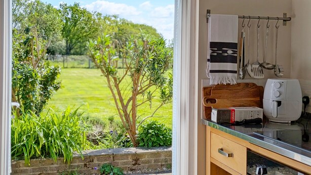 A kitchen with a view of a green garden, a wooden cutting board, a toaster, and hanging kitchen utensils. - Fewhurst Cottage Annex - Billingshurst (Billingshurst, Horsham)