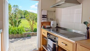 A kitchen with a view of a garden, a stove, a microwave, and a range hood. - Fewhurst Cottage Annex - Billingshurst (Billingshurst, Horsham)