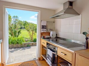 Une cuisine donnant sur un jardin, équipée d’une cuisinière, d’un four à micro-ondes et d’une hotte aspirante.