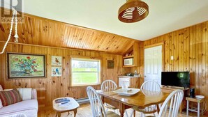 Un accogliente interno di una baita con pareti in legno, un tavolo da pranzo, sedie bianche, un divano, un televisore e una finestra con vista sull'esterno.