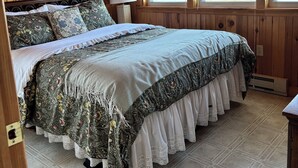 Una camera da letto con rivestimento in legno, un letto, un comodino, una lampada e finestre.