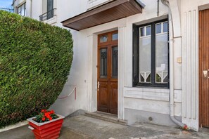 A building with a wooden door, a window with black shutters, and a neatly trimmed hedge. - Apartment 'Estaing' with Mountain View, Private Terrace and Wi-Fi (Argelès-Gazost)