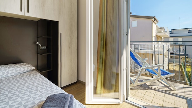 A bedroom with a bed, a wardrobe, a sliding glass door, and a balcony with a chair. - Apartment 'Villa Trentina Trilocale 2 Piano' with Shared Terrace and Wi-Fi (Jesolo)