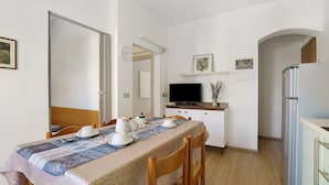 A dining area with a table set for four, a television, a refrigerator, and a wooden cabinet. - Apartment 'Villa Trentina Trilocale 2 Piano' with Shared Terrace and Wi-Fi (Jesolo)