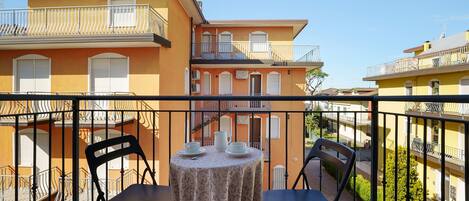 A balcony with two chairs and a table, overlooking a row of yellow buildings with balconies.