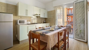 A compact kitchen with a dining table, chairs, and a view of the balcony. - Apartment 'Villa Trentina Trilocale 2 Piano' with Shared Terrace and Wi-Fi (Jesolo)