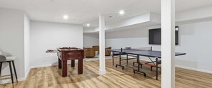 Een kamer met een tafelvoetbaltafel, een pingpongtafel en een aan de muur bevestigde televisie.