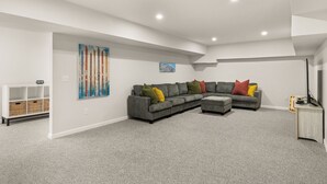 Un salon moderne avec un canapé d’angle, un téléviseur à écran plat et un tableau accroché au mur.