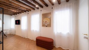 Una habitación con vigas de madera en el techo, un banco rojo y un televisor en la pared.