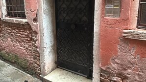 Un edificio con fachada desgastada, una puerta metálica con diseños intrincados y un ventanal con celosía de metal.