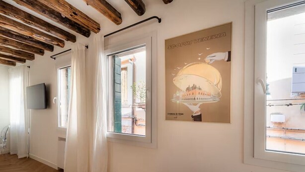 Una habitación con vigas de madera, un televisor en la pared, un cartel de un edificio y una ventana con vistas al exterior.