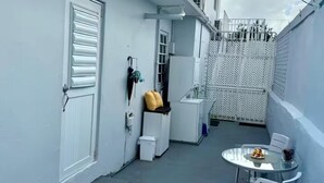 Un balcon étroit avec une porte blanche, une petite table avec des chaises et une clôture blanche.