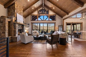 A spacious living area with a stone fireplace, wooden ceiling beams, and large windows offering views of the outdoors. - Luxe Retreat at Blue Ridge - Pool | Hot Tub | Outdoor Kitchen | Firepit | Game Room (Epworth)