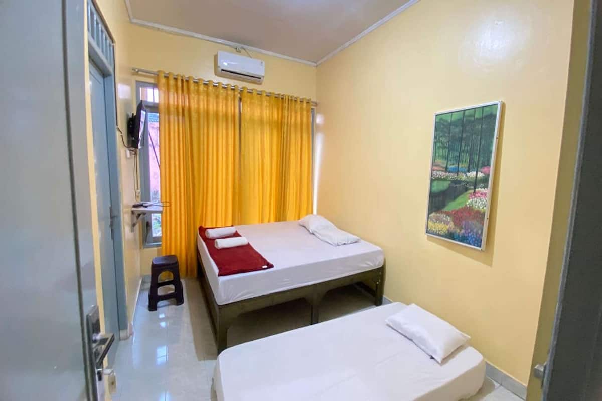 Una habitación con dos camas, una ventana con cortinas amarillas, un cuadro en la pared y un aire acondicionado.