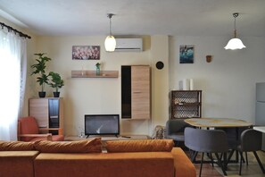 Uma sala de estar moderna com sofá, televisão, mesa de jantar com cadeiras e um vaso de planta.