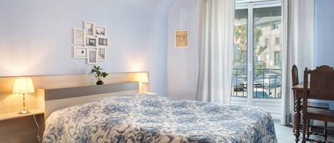 A bedroom with a bed, bedside lamps, a wall-mounted clock, a window with curtains, and a view of the outside.