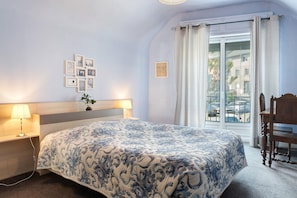 Un dormitorio con cama, lámparas de noche, un reloj en la pared, una ventana con cortinas y vistas al exterior.