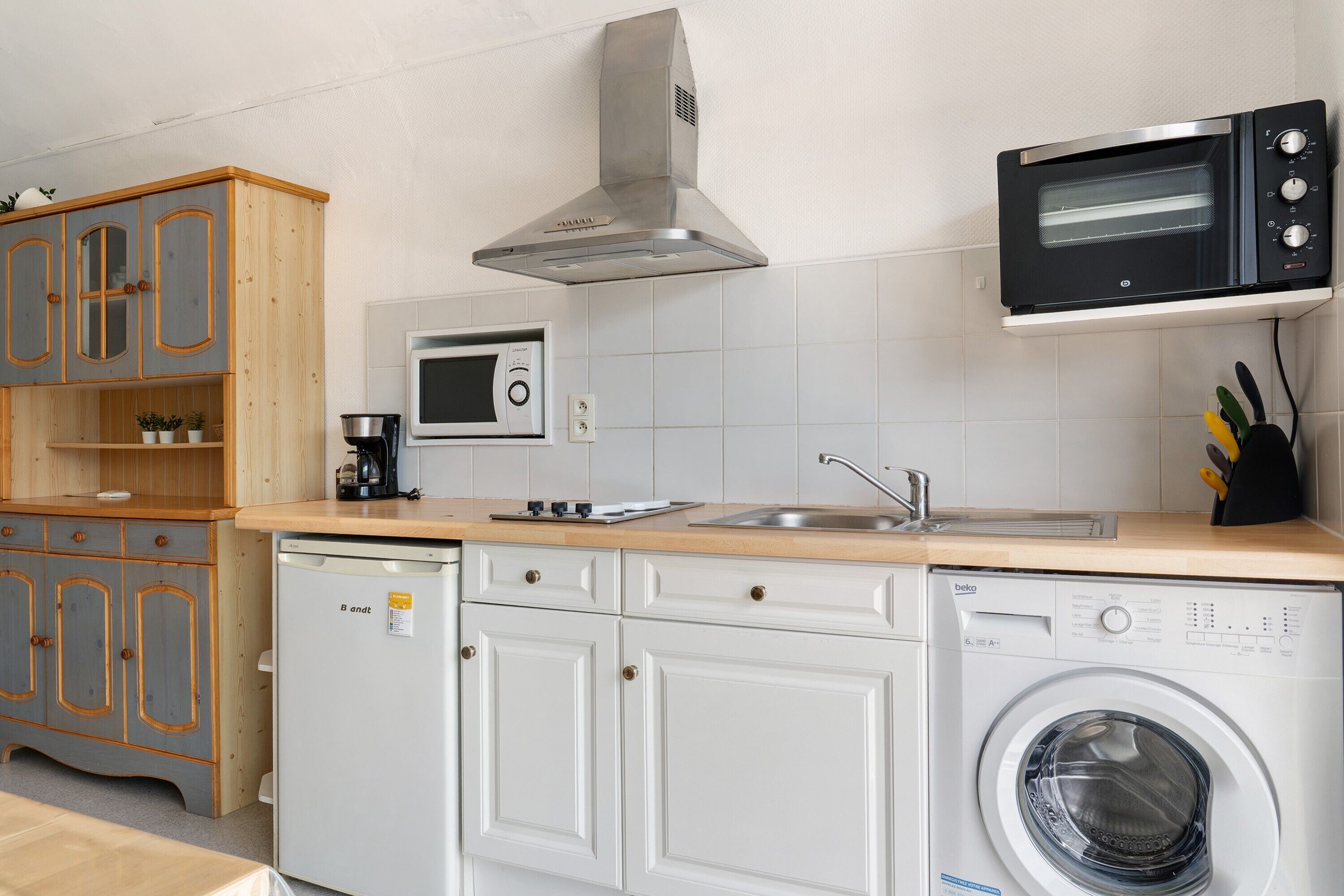 Een kleine keuken met een magnetron, broodroosteroven, vaatwasser en houten kastjes.