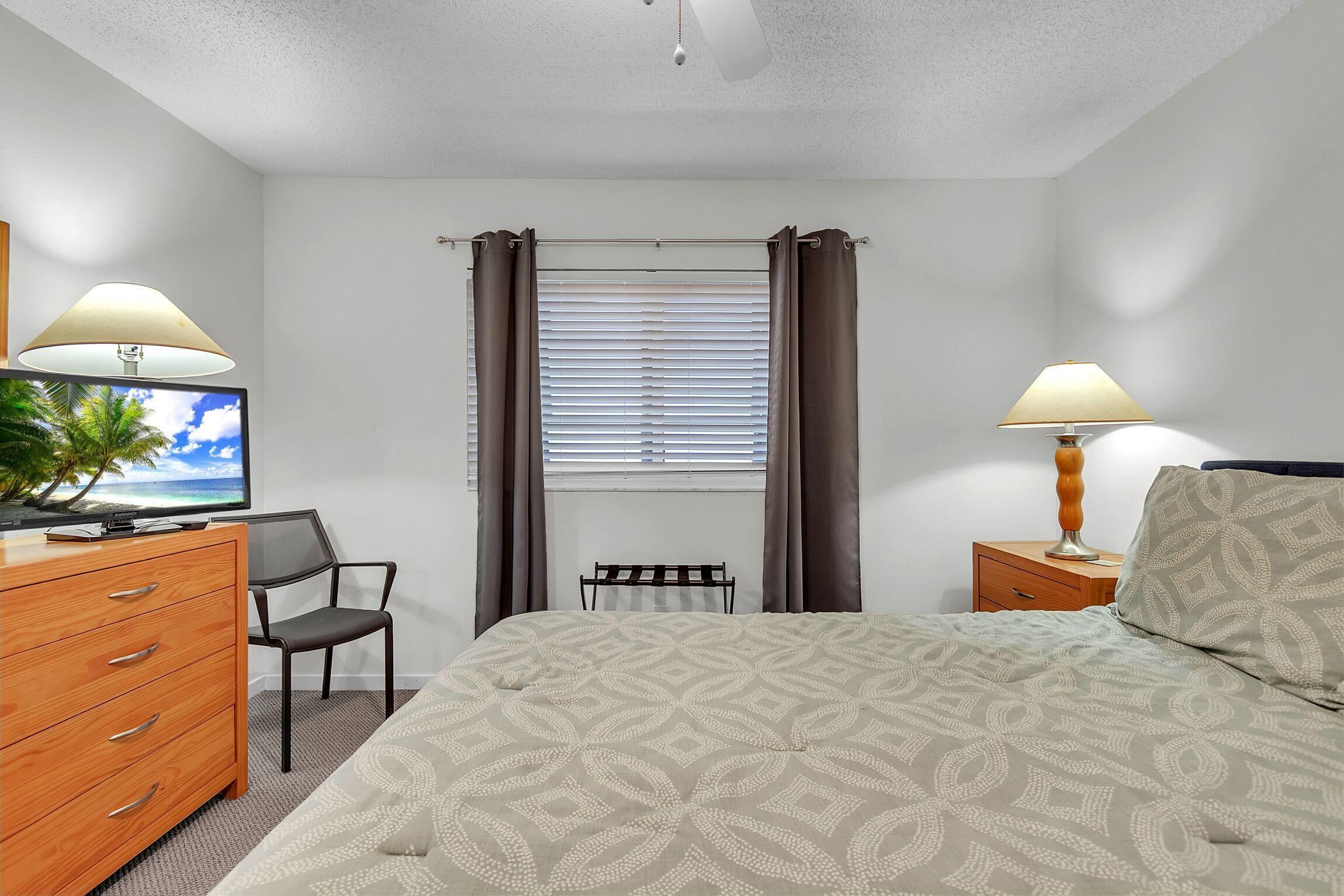 Habitación de hotel con cama, escritorio con computadora, silla, cómoda y ventana con cortinas.