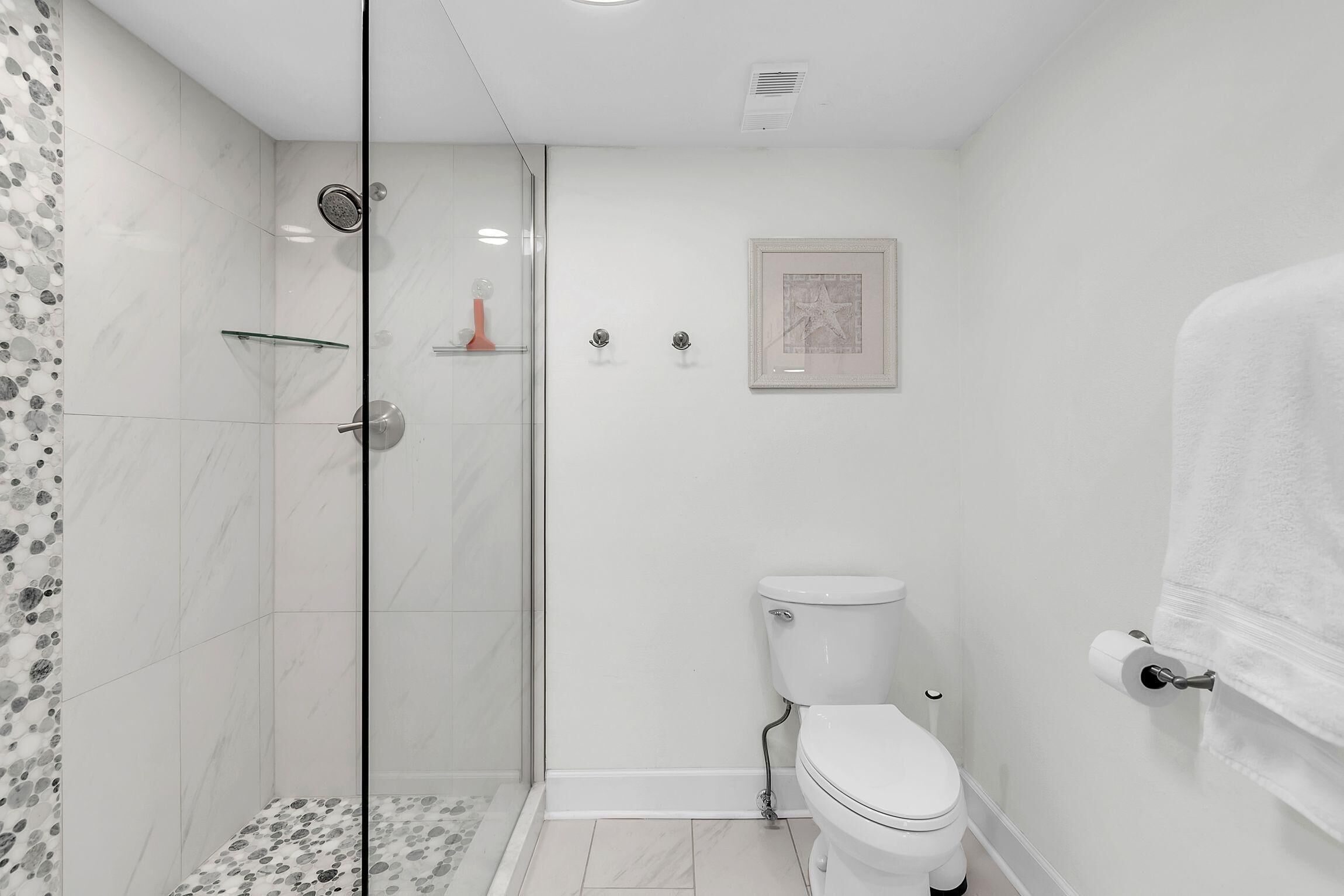 Een moderne badkamer met een douchecabine van glas, een toilet en een lijst met een foto aan de muur.