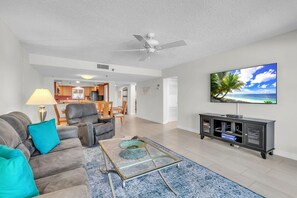 A living room with a sofa, coffee table, TV, and a view of the ocean. - Reflections On The Gulf #502 - Paradise on the Gulf (Indian Rocks Beach)