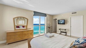 Ein Schlafzimmer mit einem großen Bett, einem Schminktisch, einem Fernseher und Meerblick.