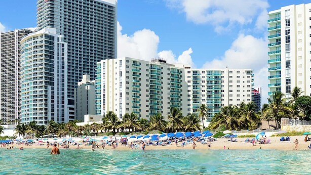 Ein Strandhotel mit mehreren Hochhäusern, einem Sandstrand und Palmen.