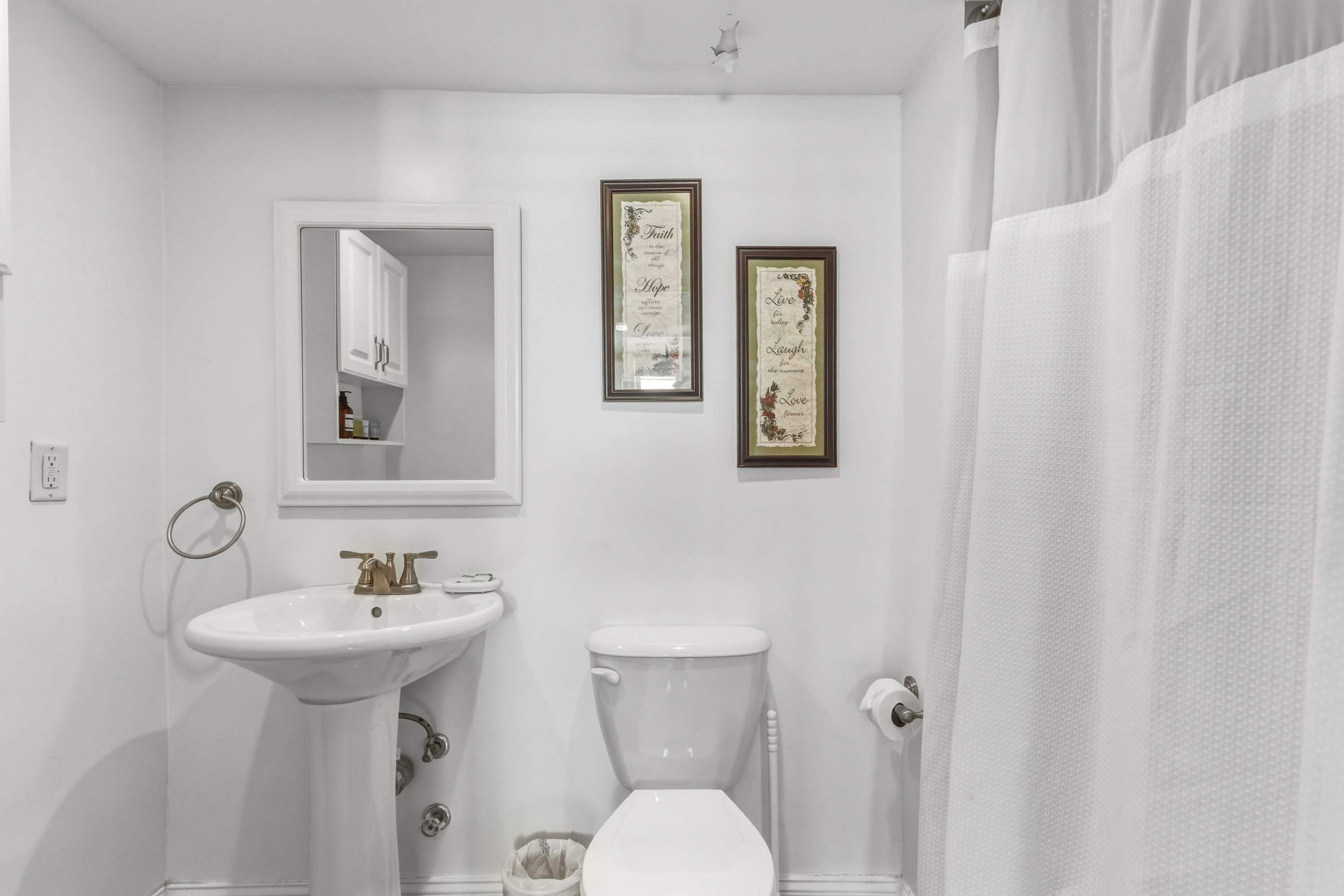 A bathroom with a pedestal sink, a toilet, a framed mirror, and two framed inspirational quotes on the wall.