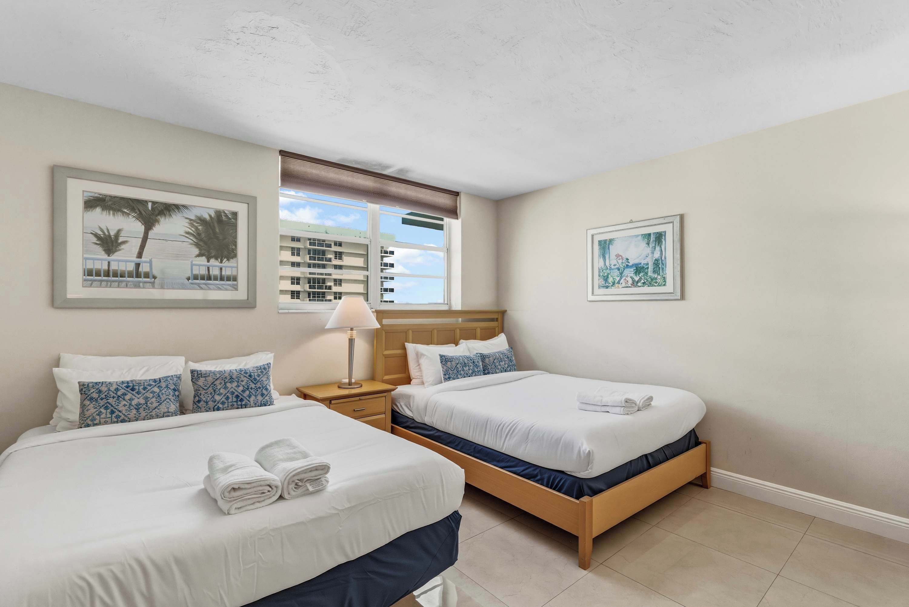 A hotel room with two beds, a nightstand, a lamp, and framed pictures on the walls.