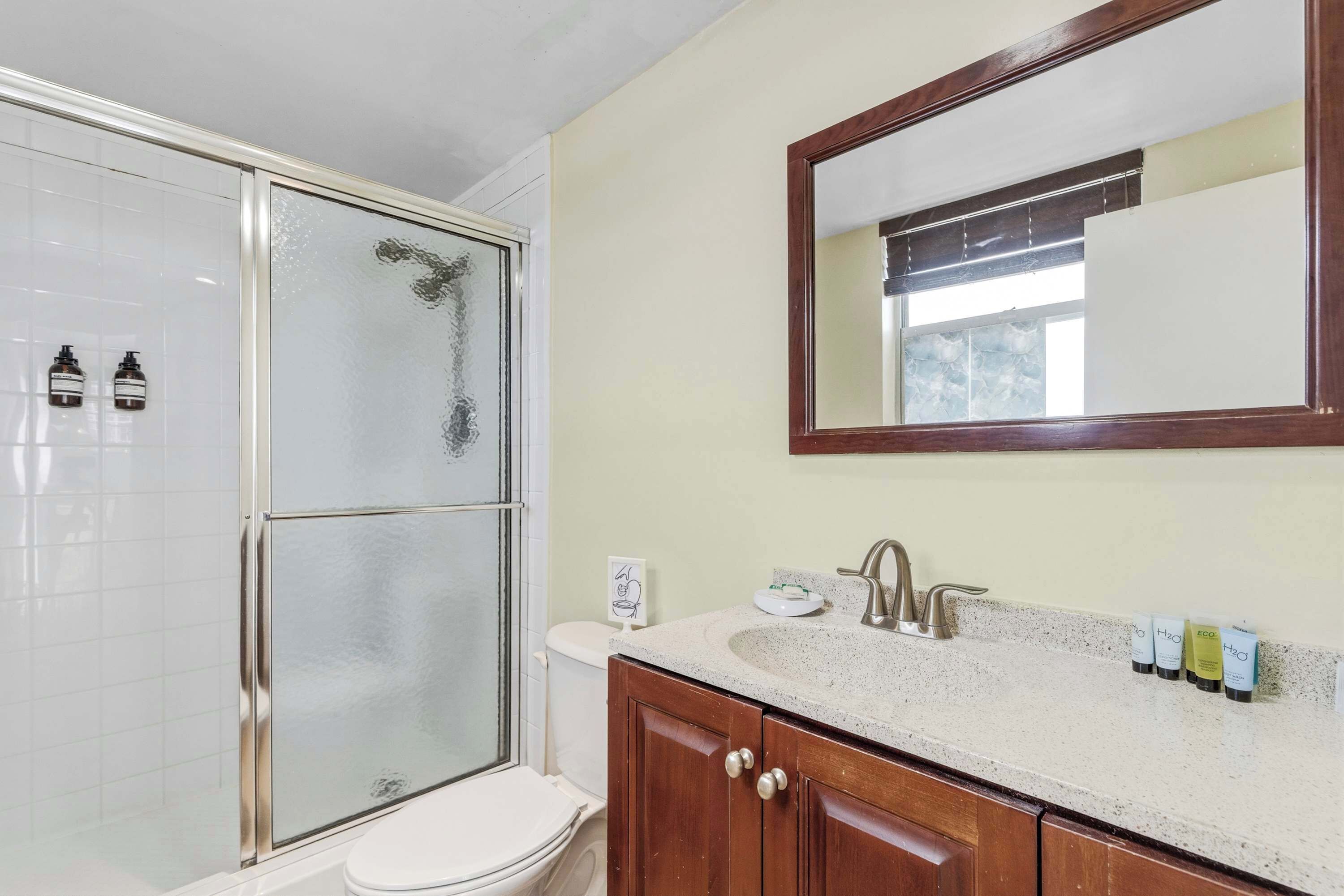 Un baño con cabina de ducha de vidrio, un lavabo con espejo y artículos de aseo en la encimera.