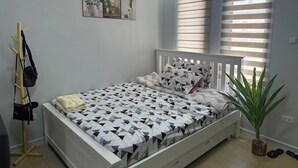 A bedroom with a bed, a coat rack, a potted plant, and a window with blinds. - Cozy 1-bedroom House Rental in Hermosa, Philippines (Hermosa)