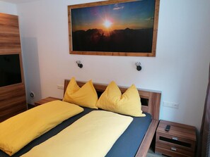 Cama com roupa de cama amarela, pintura de um pôr do sol e cabeceira de madeira.